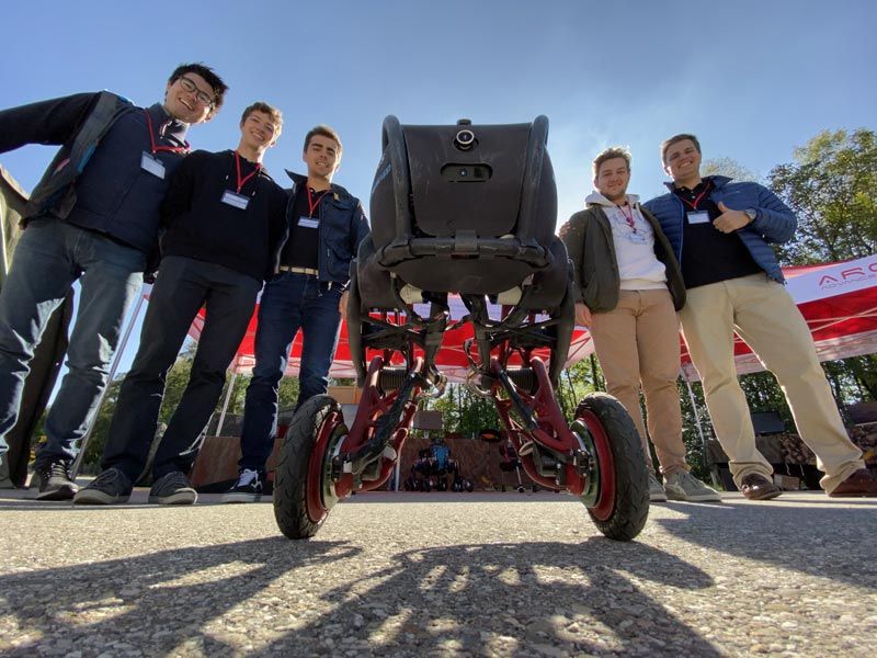 Five smiling members of the Ascento team standing outside and gathered around the robot. One member giving the thumbs-up.