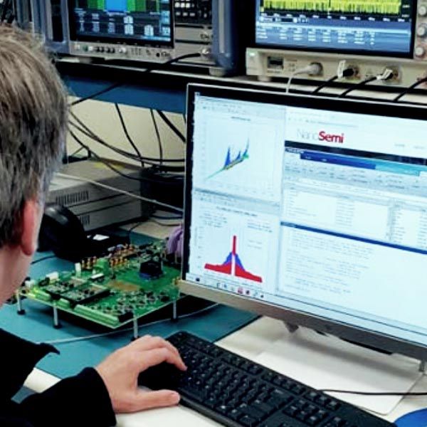 NanoSemi engineer working on computer. Rack of lab equipment in background.