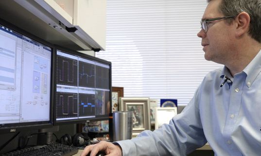 Kottenstette is seated in his office. The computer screen on the left shows Simulink Real-Time models.
